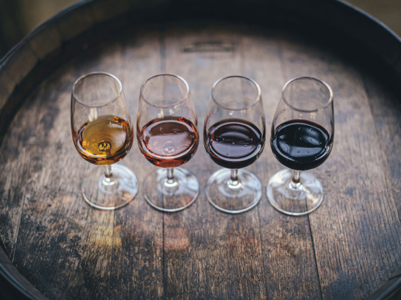 Image of four glasses of win lined up on a wooden barrel ready for wine tasting in a french vineyard.